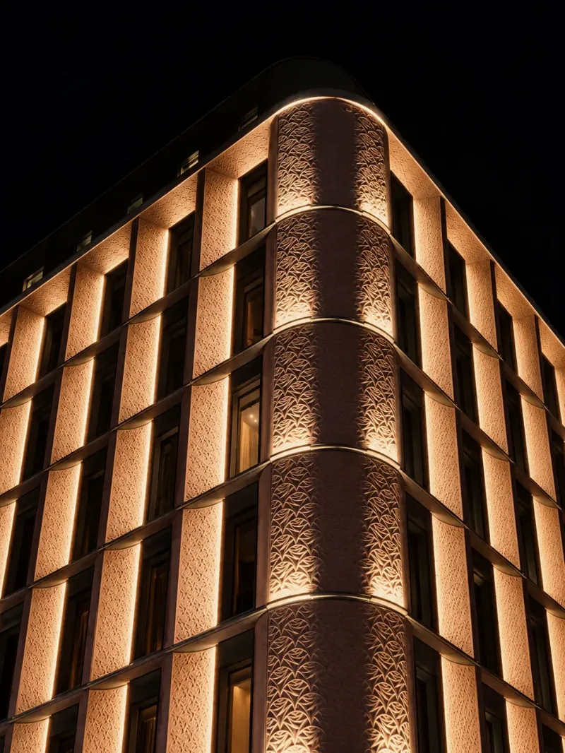 Illuminated corner of a hotel building at night, its carved stone facade lit between dark windows